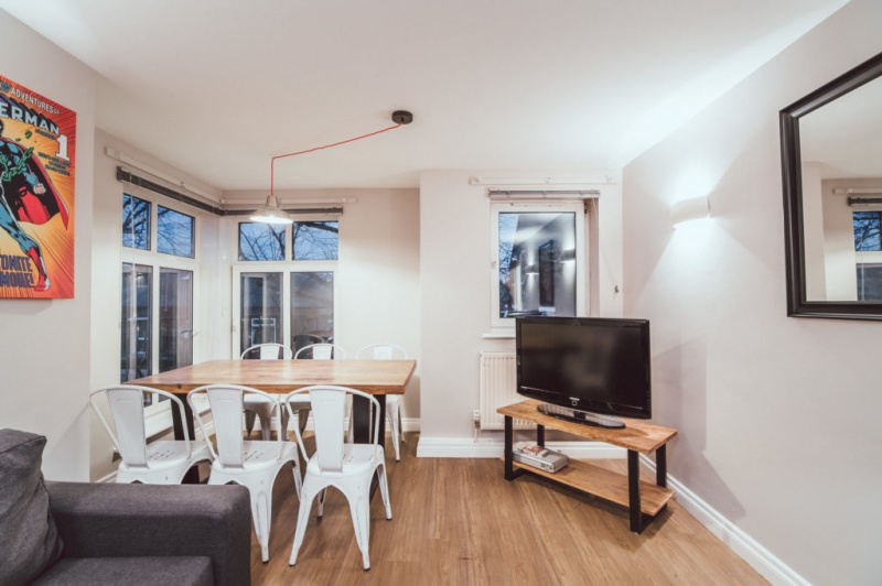 Dining area with a wooden table, white chairs, and a TV in a cozy living space.