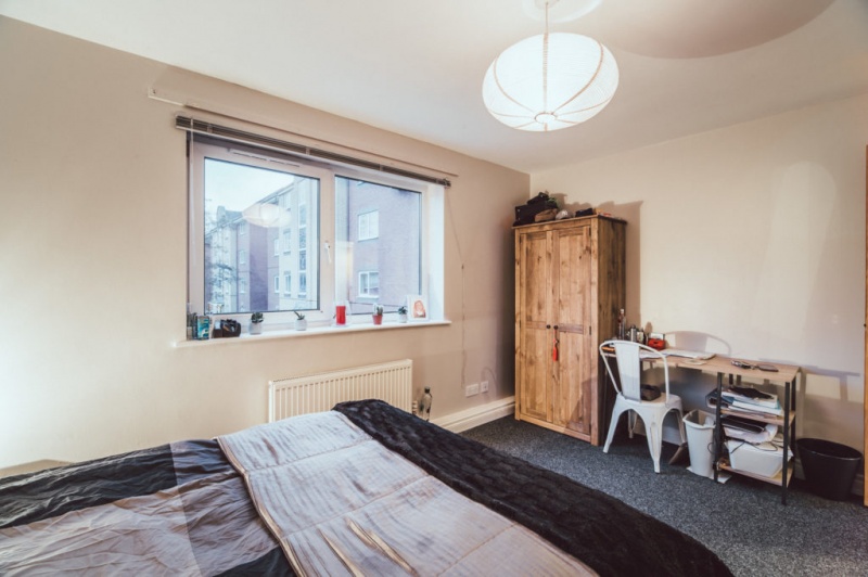 Bright bedroom with a large bed, wooden wardrobe, and study desk by the window 