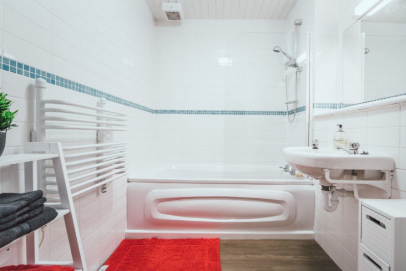 White-tiled bathroom with a bathtub, sink, and a red rug.