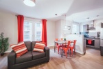 mMayfair Court Bright living space with red curtains, a small dining table, and a kitchen area.