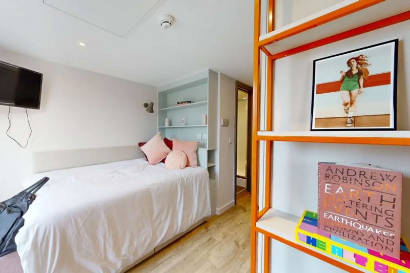 A cozy single bedroom at Cosmos Sheffield accommodation with a wall-mounted TV and shelves.