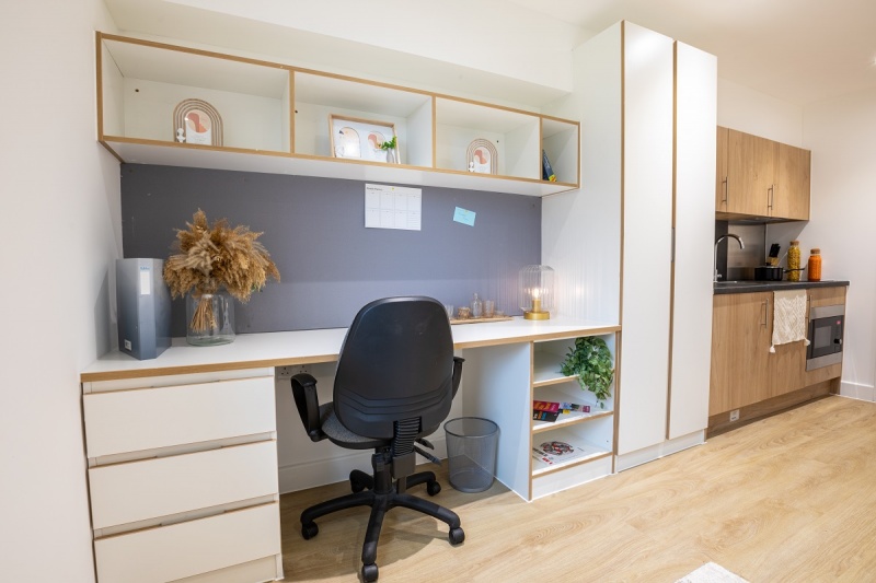 A tidy workspace in a premium townhouse studio featuring a desk, chair, and shelves for storage