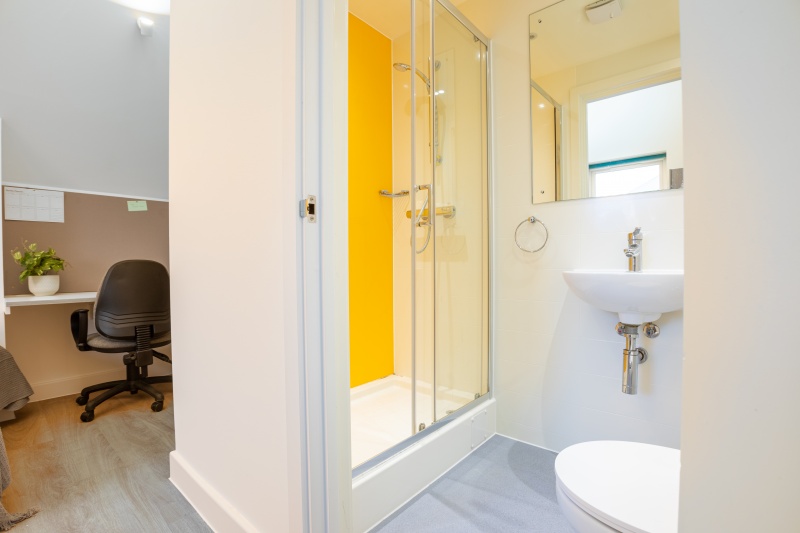 A clean and contemporary bathroom in a townhouse deluxe studio featuring a walk-in shower, sink, and