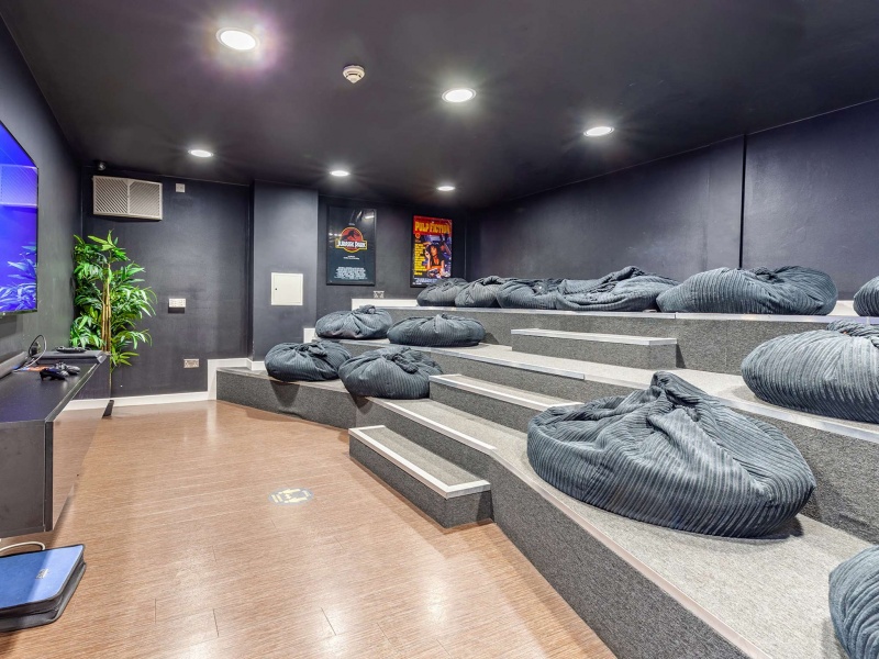 A dark cinema room with bean bag seating, a large screen, and movie posters on the walls.