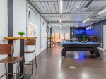 A modern games room with a pool table, bar-style seating, and a neon sign that reads 