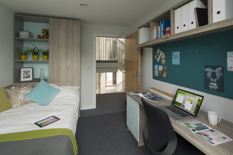 Student bedroom with a bed, study desk, and shelving unit, overlooking a staircase.